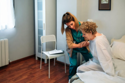 caregiver helping senior woman to get out of bed